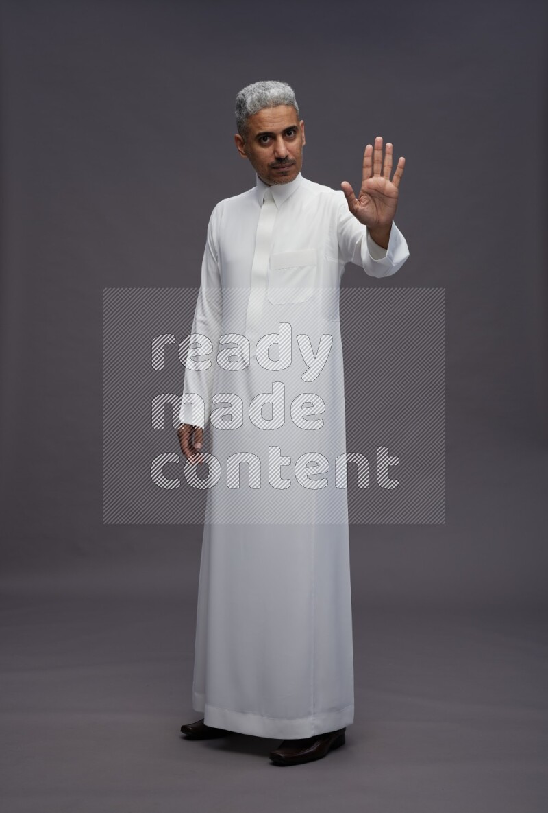 Saudi man wearing thob standing interacting with the camera on gray background