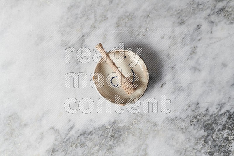 Multicolored Pottery bowl with wooden honey handle in it, on grey marble flooring, Top View