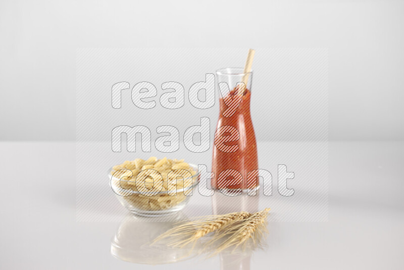 Raw pasta with tomatoe pasta with different ingredients such as cherry tomatoes, basil, garlic, bay laurel, cardamom, white pepper, black pepper, red chilis and wheat stalks on light grey background