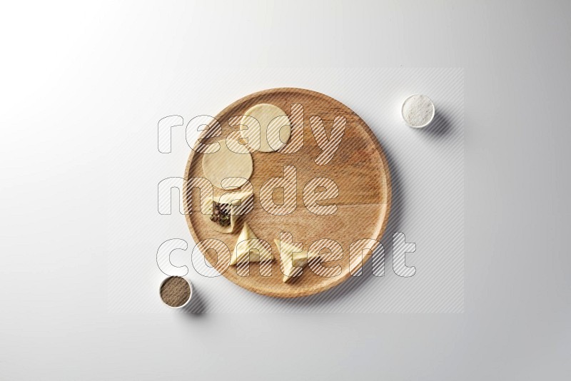 two closed sambosas and one open sambosa filled with meat while salt and black pepper aside in a wooden dish on a white background