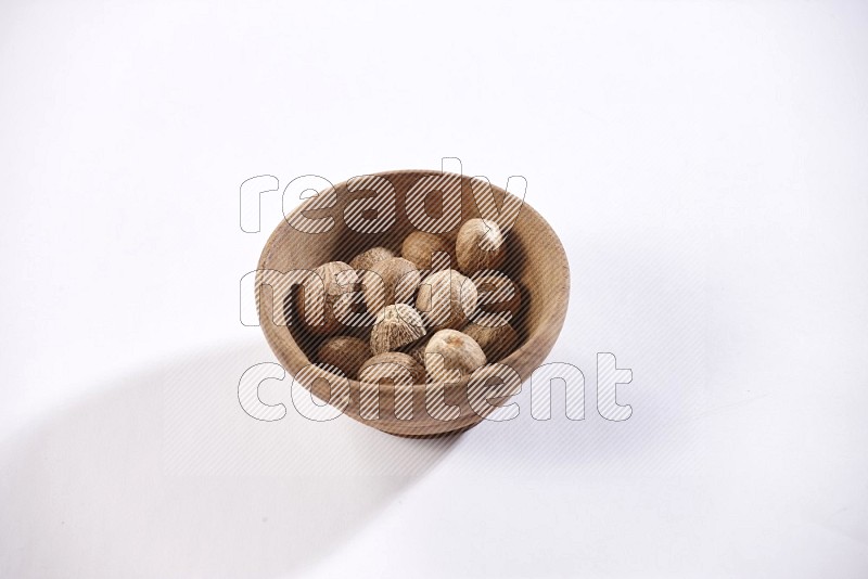 A wooden bowl full of nutmeg on a white flooring in different angles