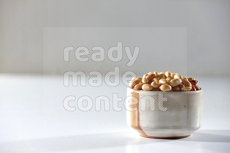 A beige ceramic bowl full of peeled peanuts on a white background in different angles