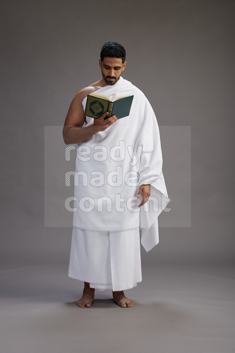 A man wearing Ehram Standing reading quran on gray background