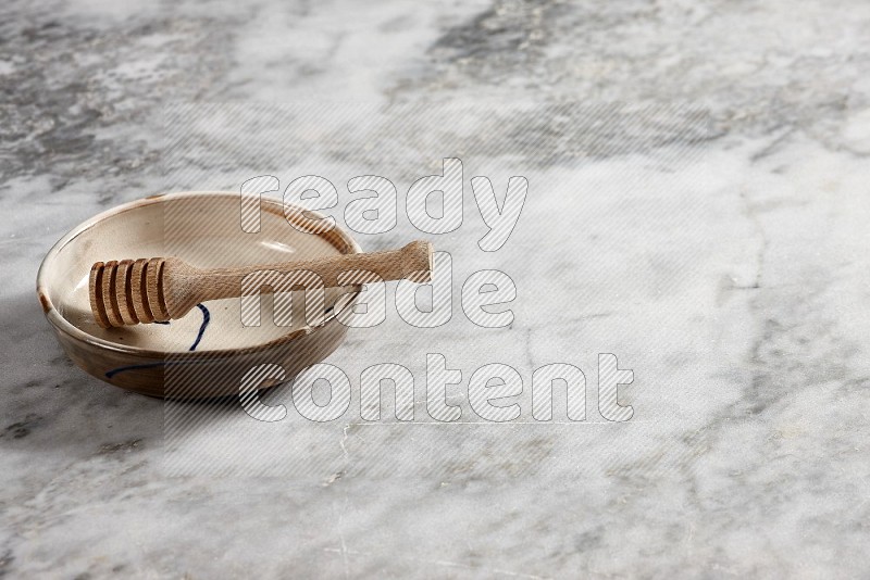 Multicolored Pottery bowl with wooden honey handle in it, on grey marble flooring, 45 degree angle