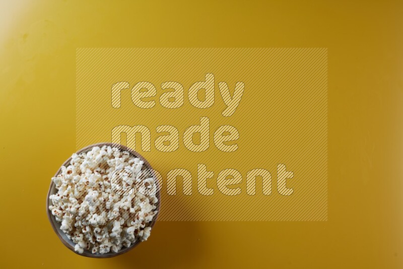 A brown pottery bowl full of popcorn on a yellow background in different angles