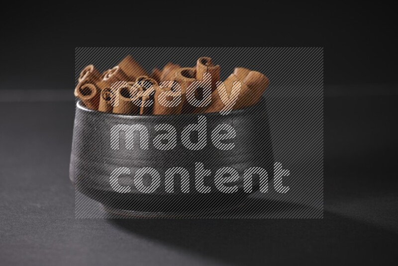Cinnamon sticks in a black bowl on a black background in different angles