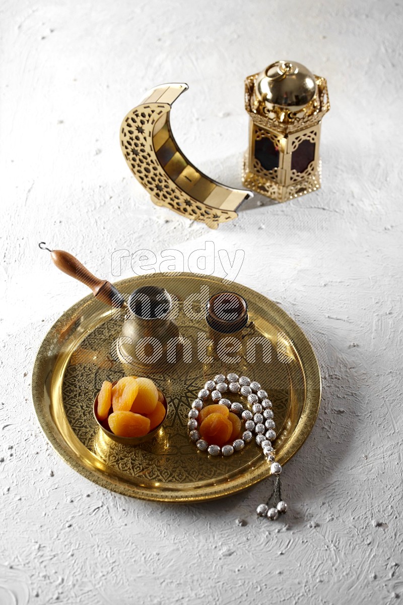 Dried apricots in a metal bowl with coffee and prayer beads on a tray beside lanterns in a light setup