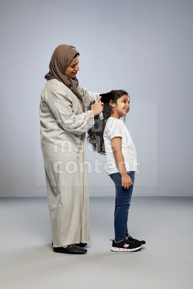 Mom standing styling hair for her daughter on gray background