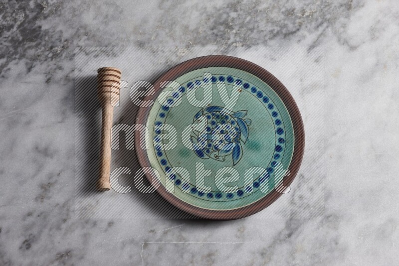 Decorative pottery plate with wooden honey dipper on the side on grey marble background