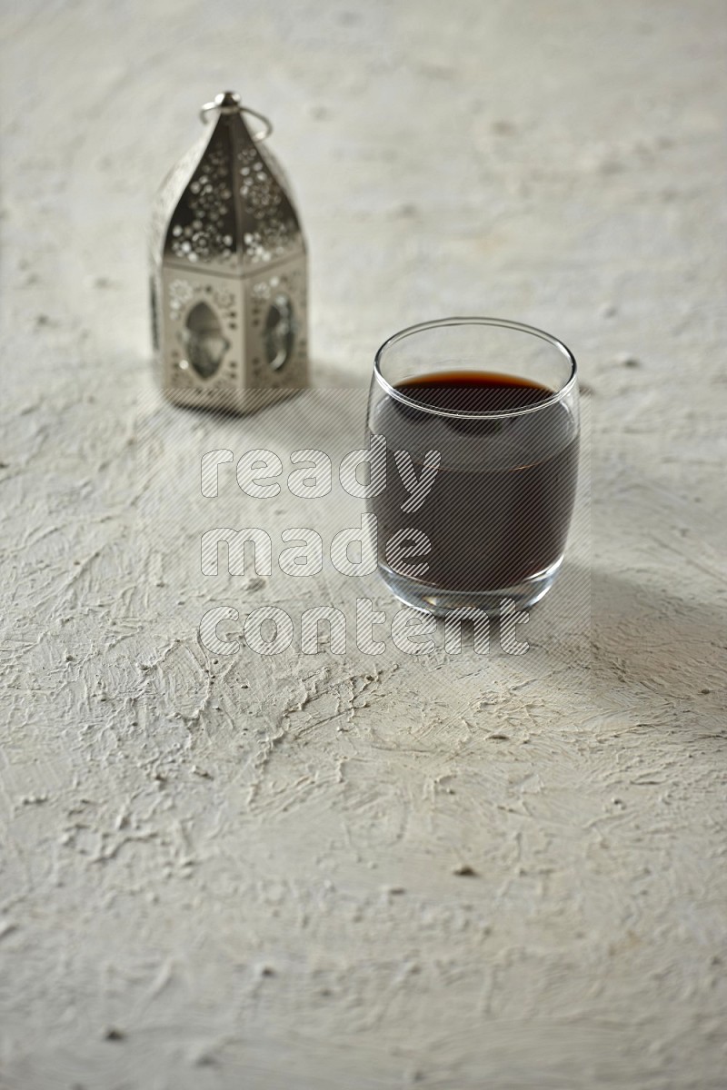 A silver lantern with different drinks, dates, nuts, prayer beads and quran on textured white background