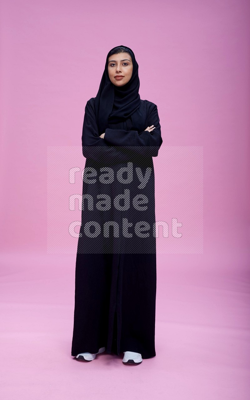 Saudi woman wearing Abaya standing with crossed arms on pink background