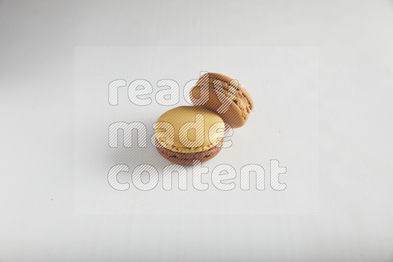 45º Shot of of two assorted Brown Irish Cream, and Yellow, and Brown Chai Latte macarons on white background