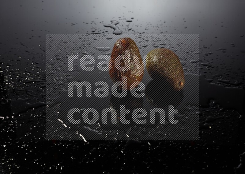 A whole avocado on black background with water drops.