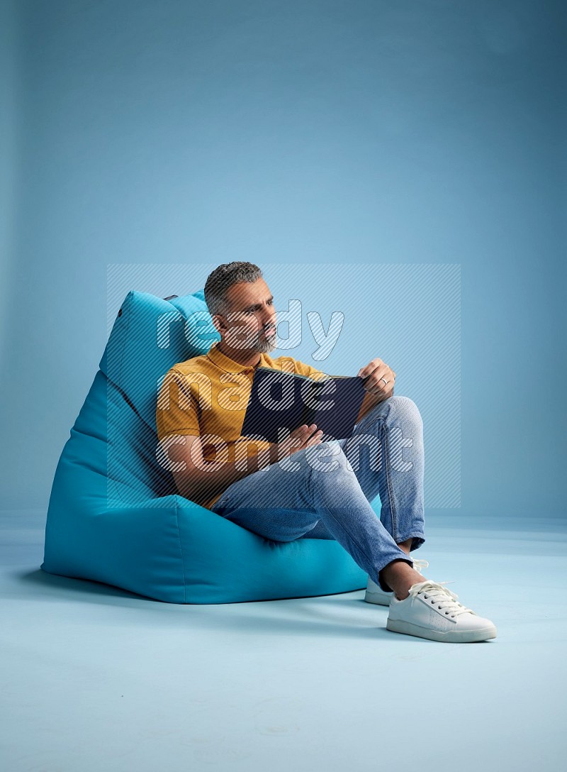 A man sitting on a blue beanbag and reading a book