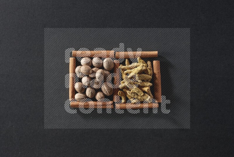 مربعان من أعواد القرفة ممتلئان بجوزة الطيب وأصابع الكركم علي خلفية سوداء