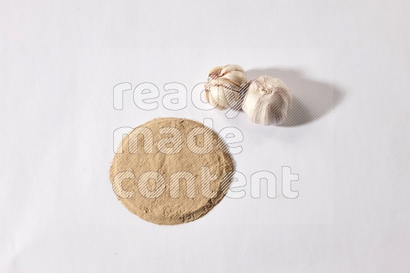 Garlic powder in a circle shape and beside it 2 garlic bulbs on a white flooring in different angles