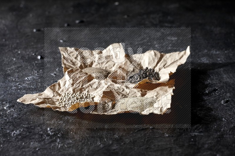 Crumpled pieces of paper full of black and white pepper beads and powder on a textured black flooring