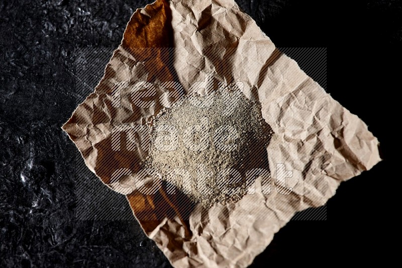 White pepper powder in a crumpled paper on textured black flooring