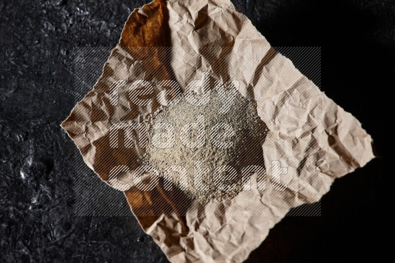 White pepper powder in a crumpled paper on textured black flooring