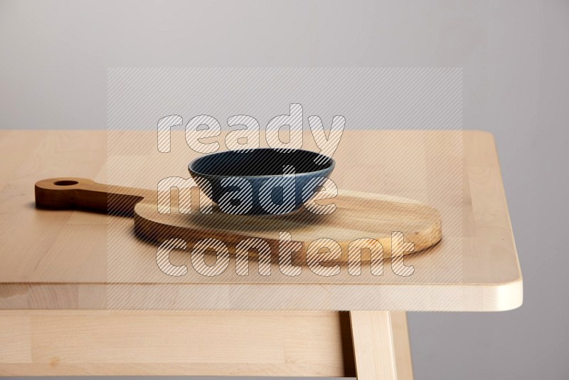 blue bowl placed on a  wooden oval cutting board on the edge of wooden table