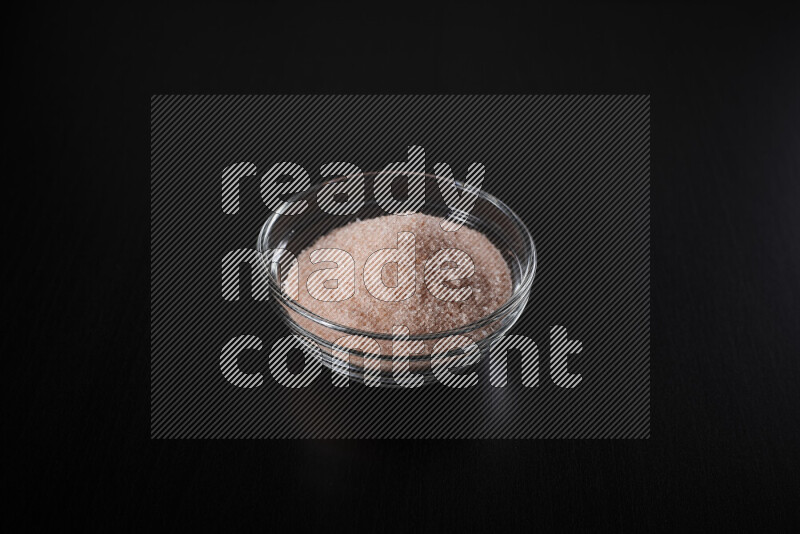 A glass bowl full of fine himalayan salt on black background