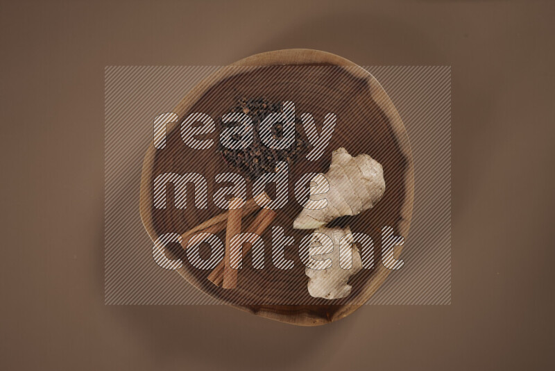 An assorted whole spices on a flat wooden tray including fresh and dried ginger, cinnamon sticks, cardamom, turmeric fingers, cloves, star anise on beige background