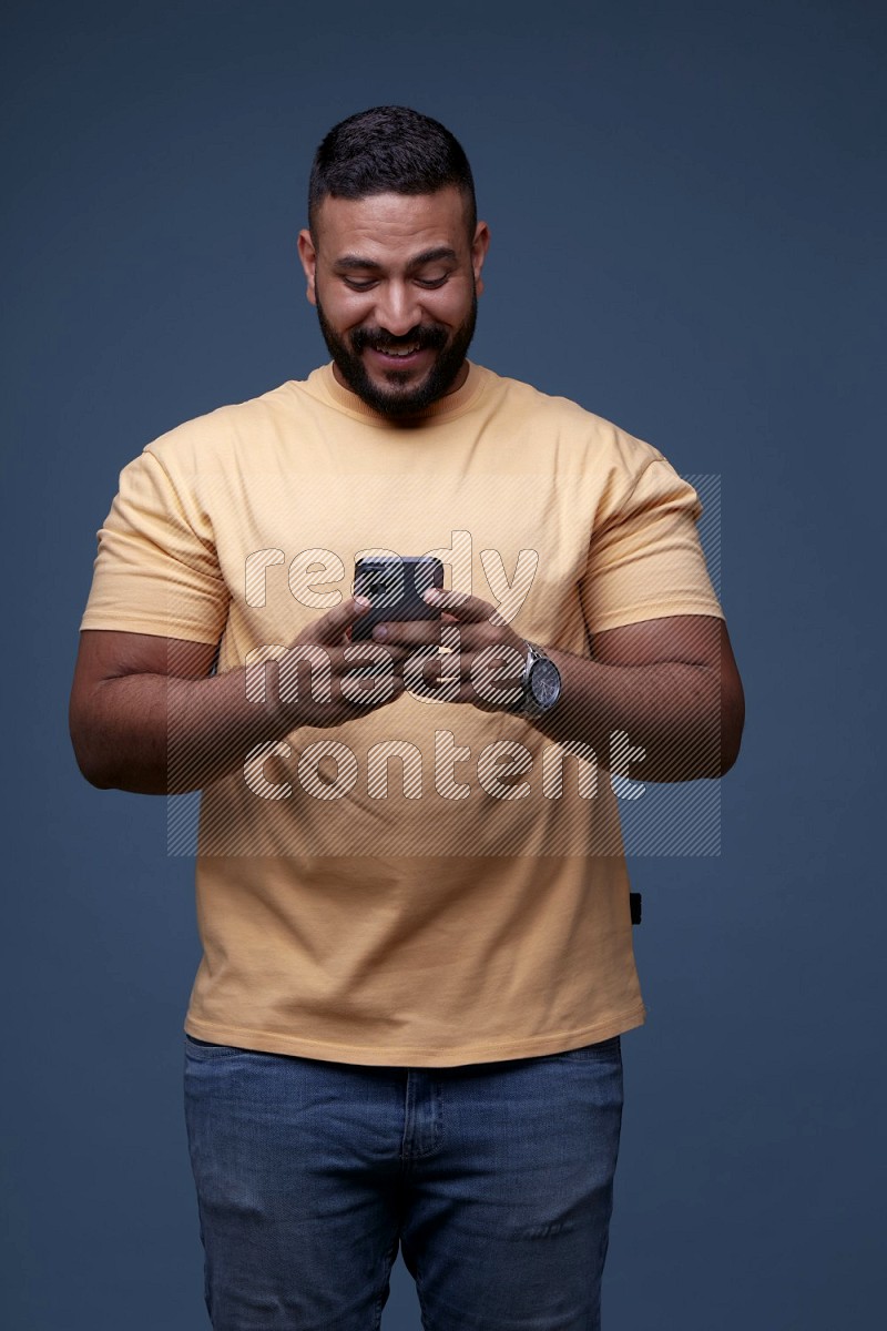 A man Texting on his phone on Blue Background wearing Orange T-shirt