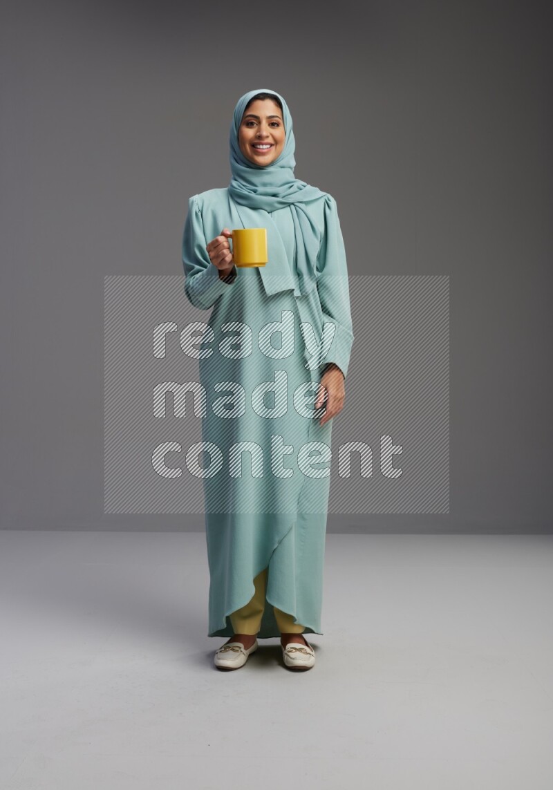 Saudi Woman wearing Abaya standing  holding a mug on Gray background