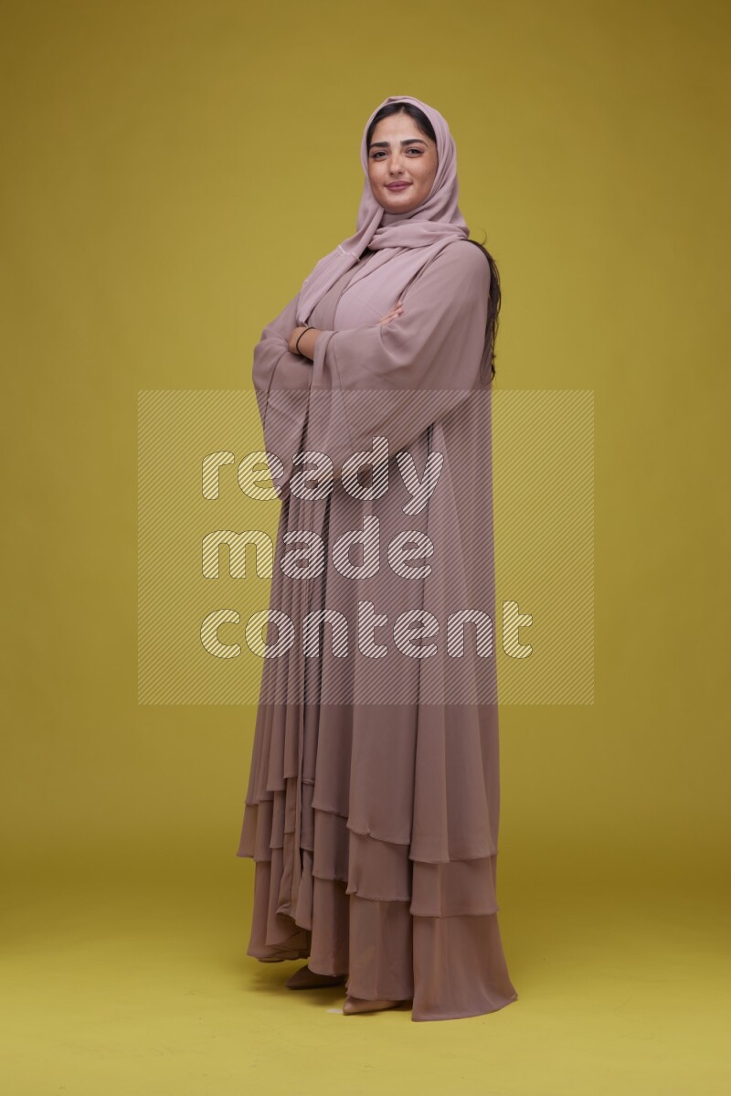 A woman Posing on a Yellow Background wearing Brown Abaya with Hijab
