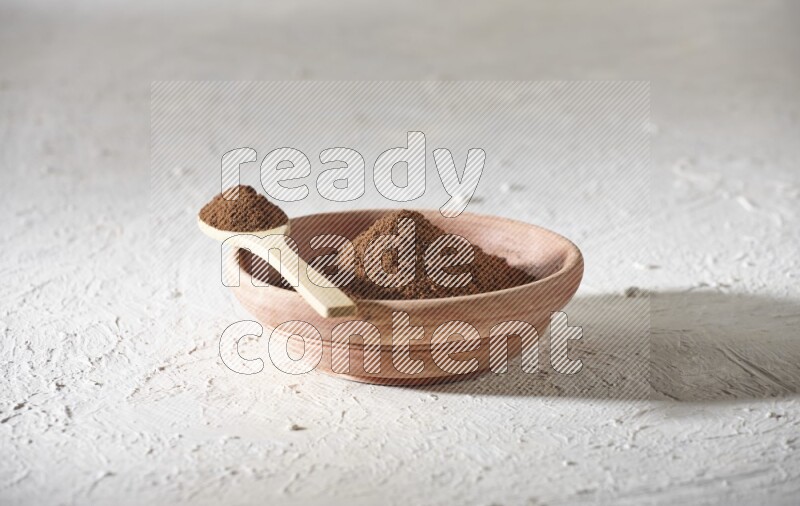 A wooden bowl and a wooden spoon full of cloves powder on a textured white flooring