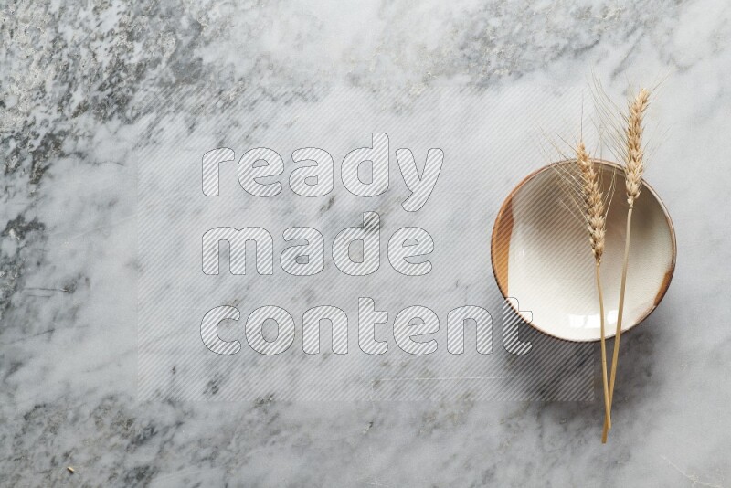 Wheat stalks on multicolored pottery plate on grey marble background