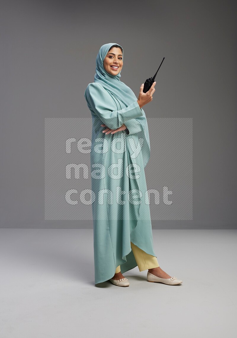 Saudi Woman wearing Abaya standing holding walkie-talkie on Gray background