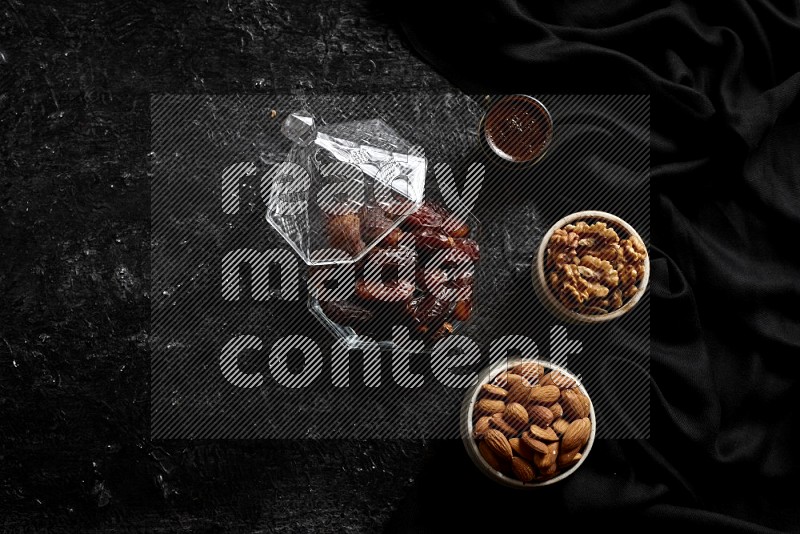 Dates in glass bowl with coffee and nuts in a dark setup