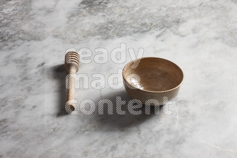 Beige pottery bowl with wooden honey dipper on the side on grey marble background