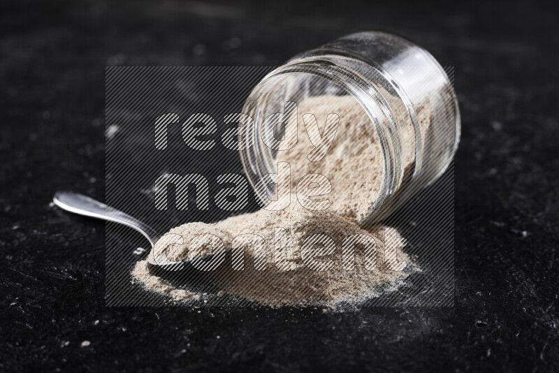 A glass jar full of onion powder flipped with some spilling powder on black background