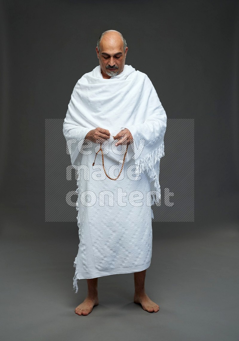 A man wearing Ehram Standing holding rosary on gray background