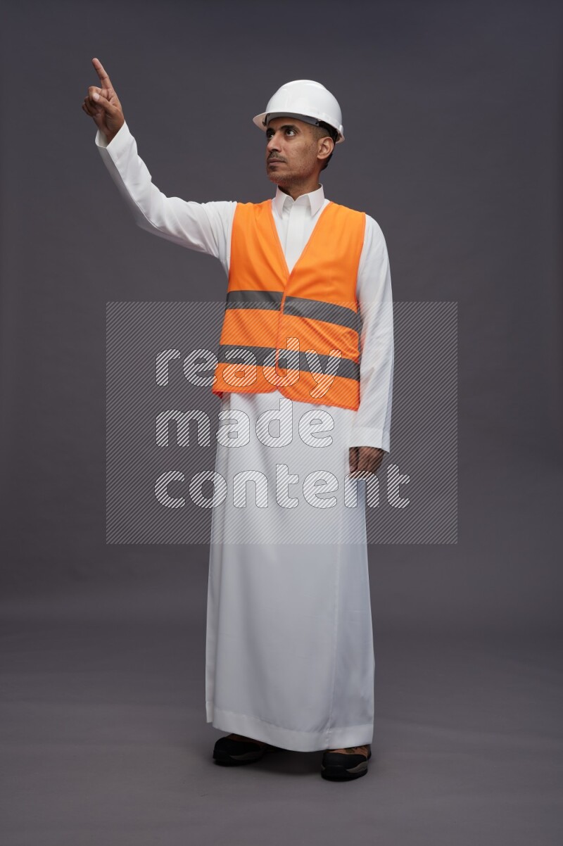 Saudi man wearing thob with engineer vest standing interacting with the camera on gray background