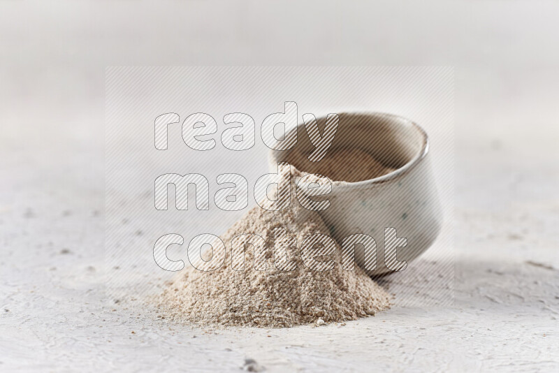 A beige pottery bowl full of onion powder with fallen powder from it on white background