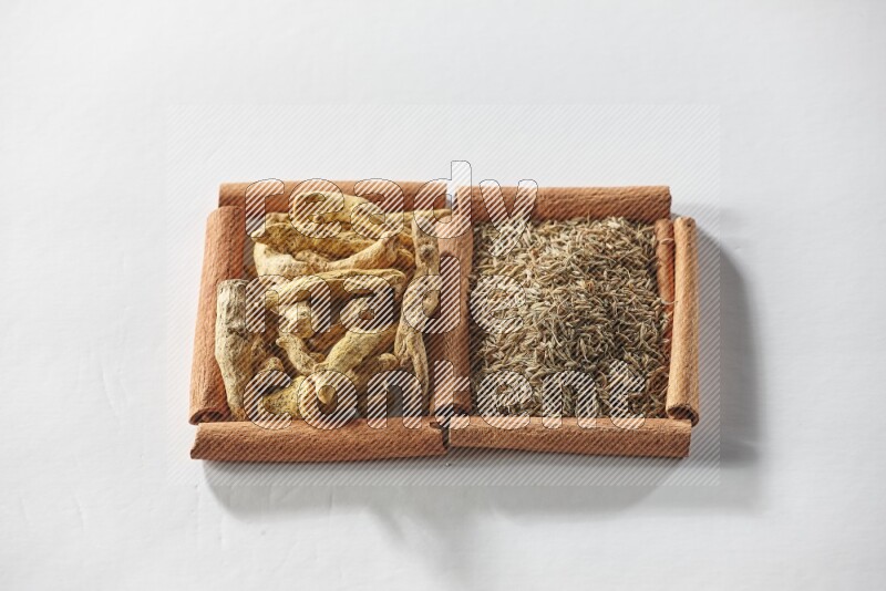 مربعان من أعواد القرفة ممتلئان بحبوب الكمون وأصابع الكركم علي خلفية بيضاء