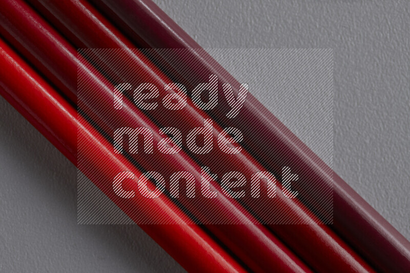 A collection of sharpened colored pencils arranged showcasing a gradient of red hues on grey background