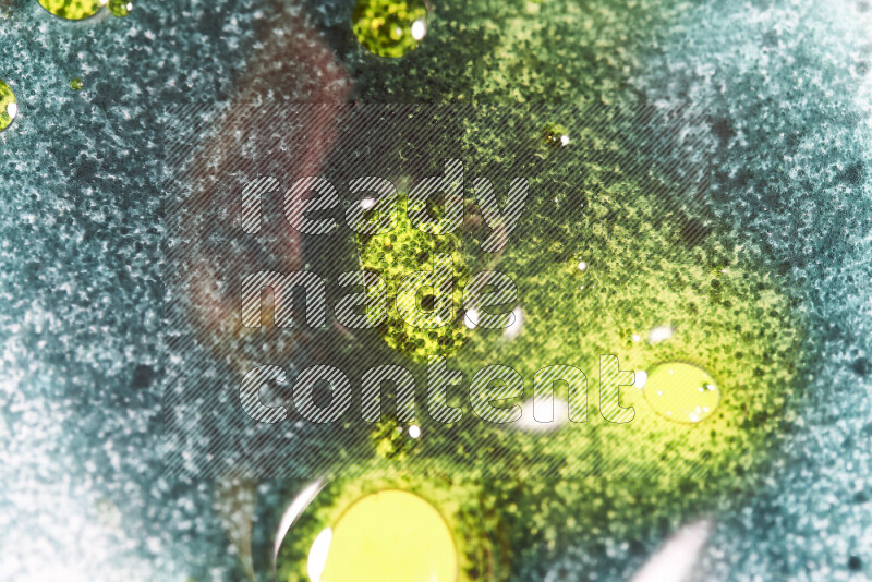 لقطات مقربة لقطرات ألوان مائية خضراء وصفراء على سطح الزيت على خلفية بيضاء