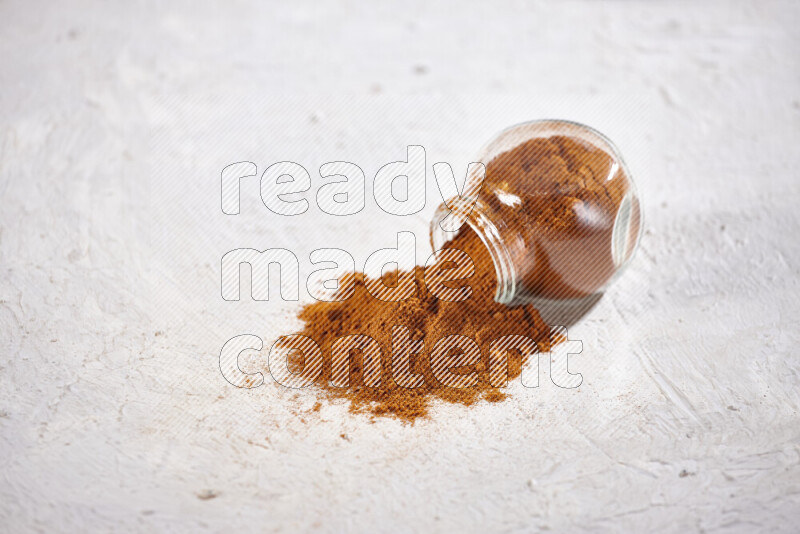 A glass jar full of ground paprika powder flipped with some spilling powder on white background