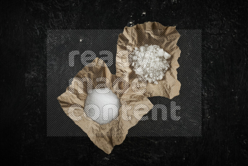 A crumpled piece of paper full of white salt on black background
