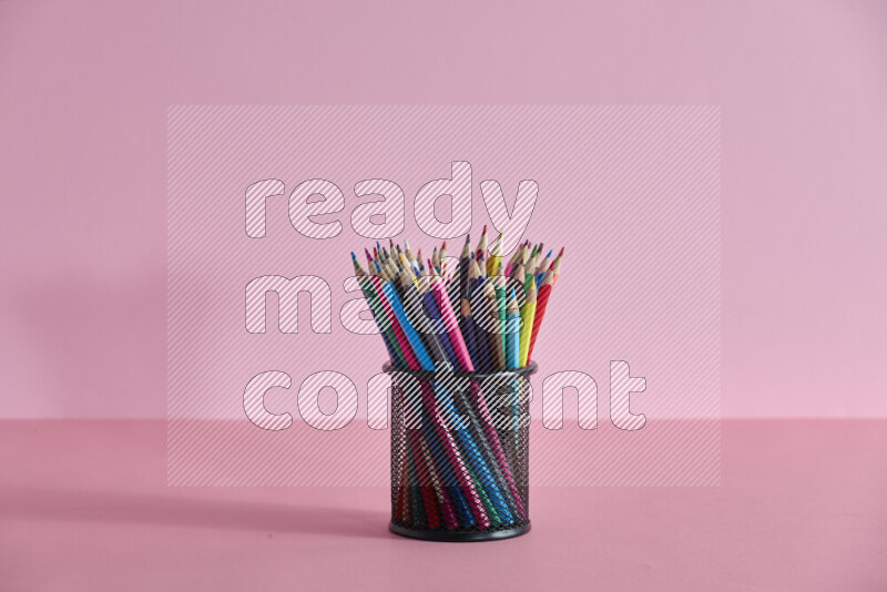Pens, pencils and other different school supplies in a metal pen holder on rose background