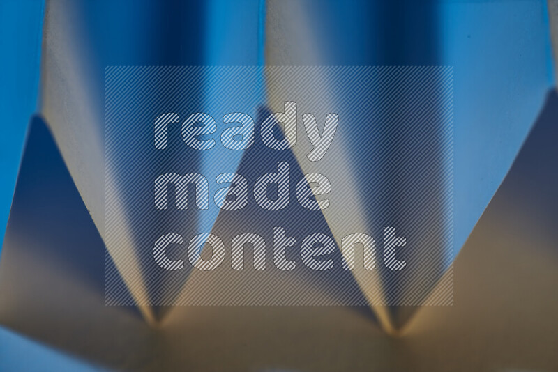 A close-up abstract image showing sharp geometric paper folds in blue gradients and warm tones