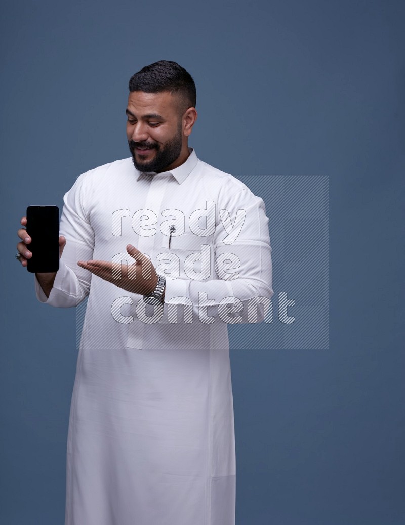 رجل سعودي يرتدي ثوب ابيض ويشير الى جواله