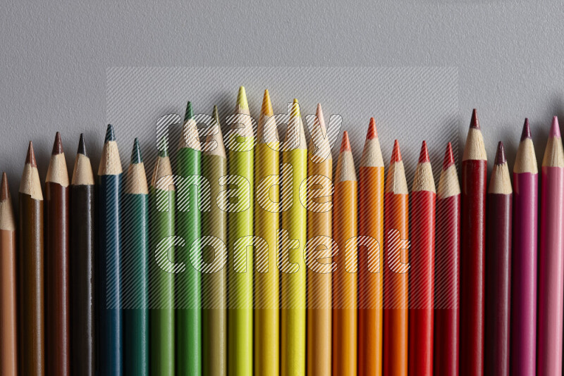 A collection of colored pencils arranged showcasing a gradient of different hues on grey background