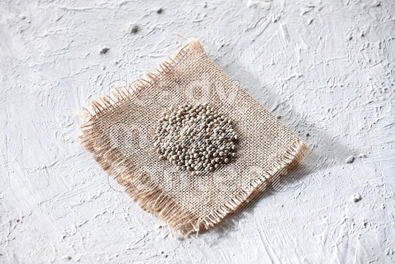 White pepper beads on a burlap piece of fabric on textured white flooring