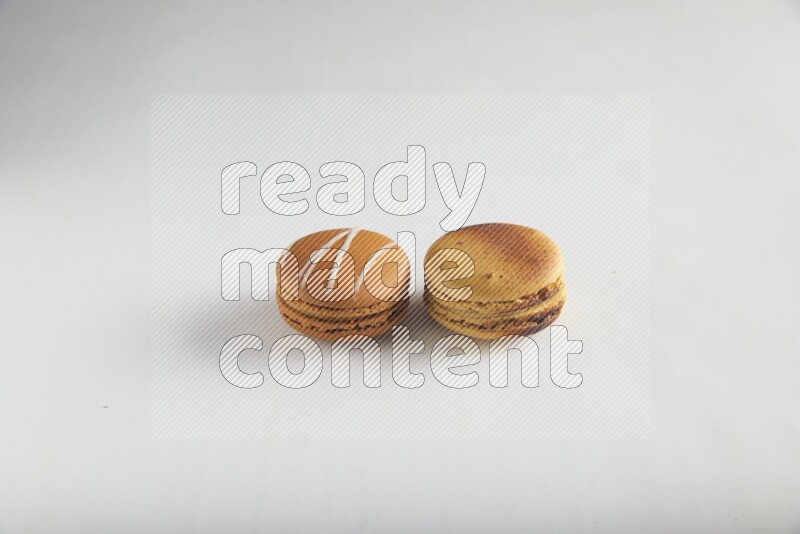 45º Shot of of two assorted Brown Irish Cream, and Yellow Crème Brulée macarons on white background