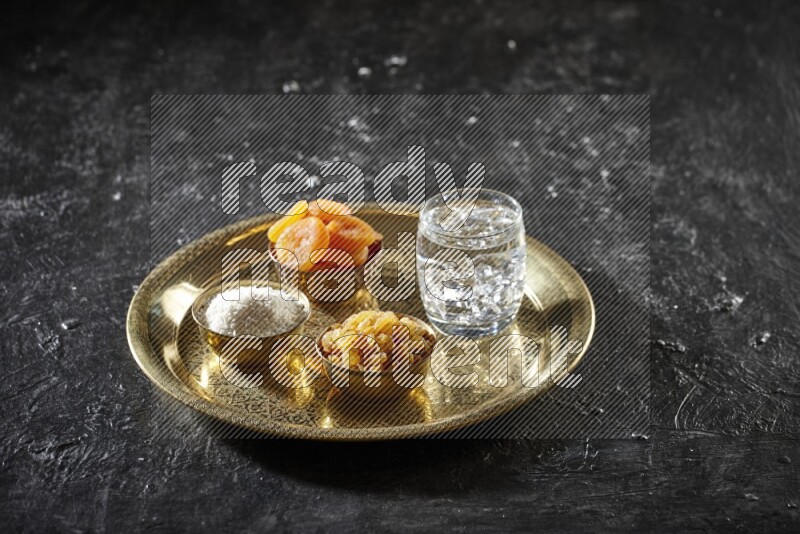 Dried fruits in metal bowls with water on a tray in dark setup